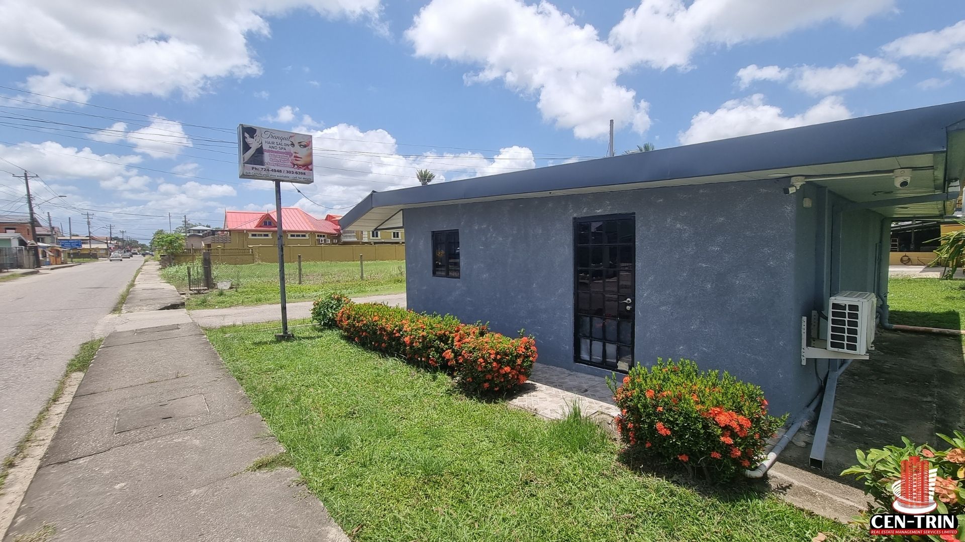A side view of the gray commercial rental building on Chin Chin Road, showing the sidewalk and an external AC unit.
