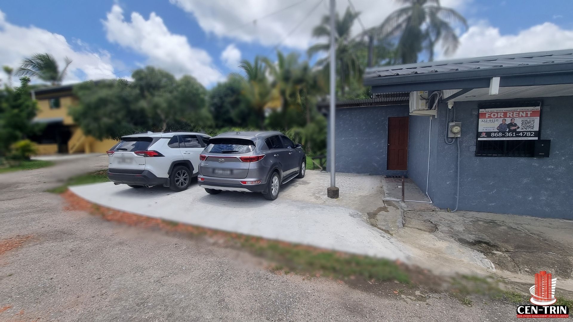 A view of the front of the gray commercial rental building on Chin Chin Road, showing the entrance, parking area, and a