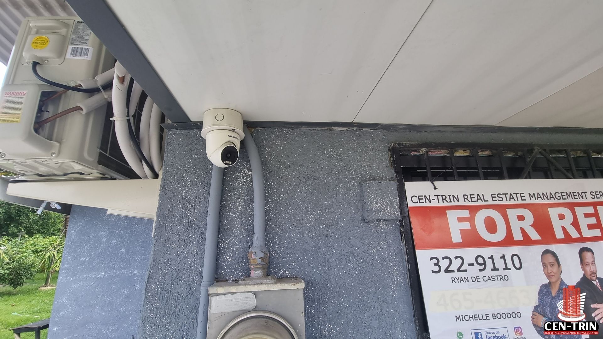 Close-up of a security camera and an AC unit mounted on the wall of the commercial rental building on Chin Chin Road.