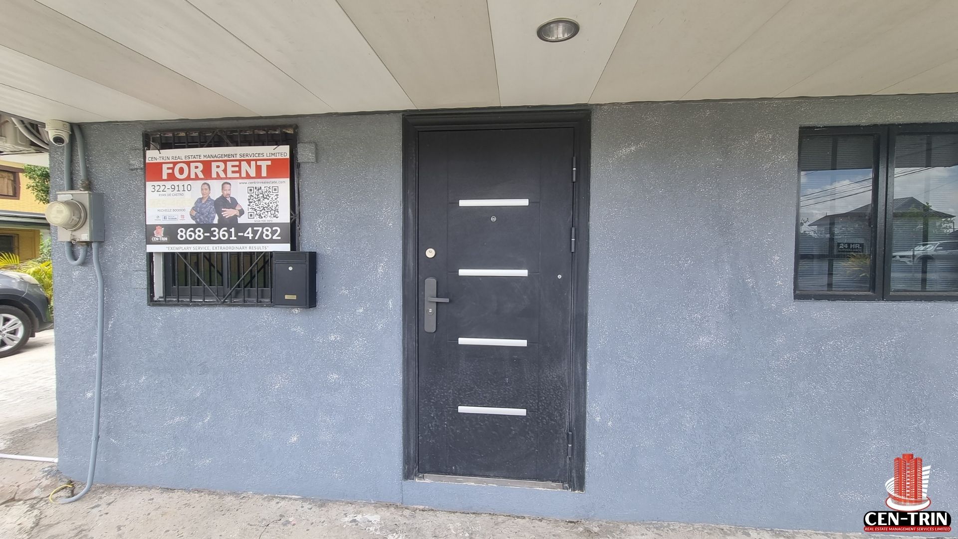 A head-on view of a gray commercial rental building on Chin Chin Road, showing the black security door and a