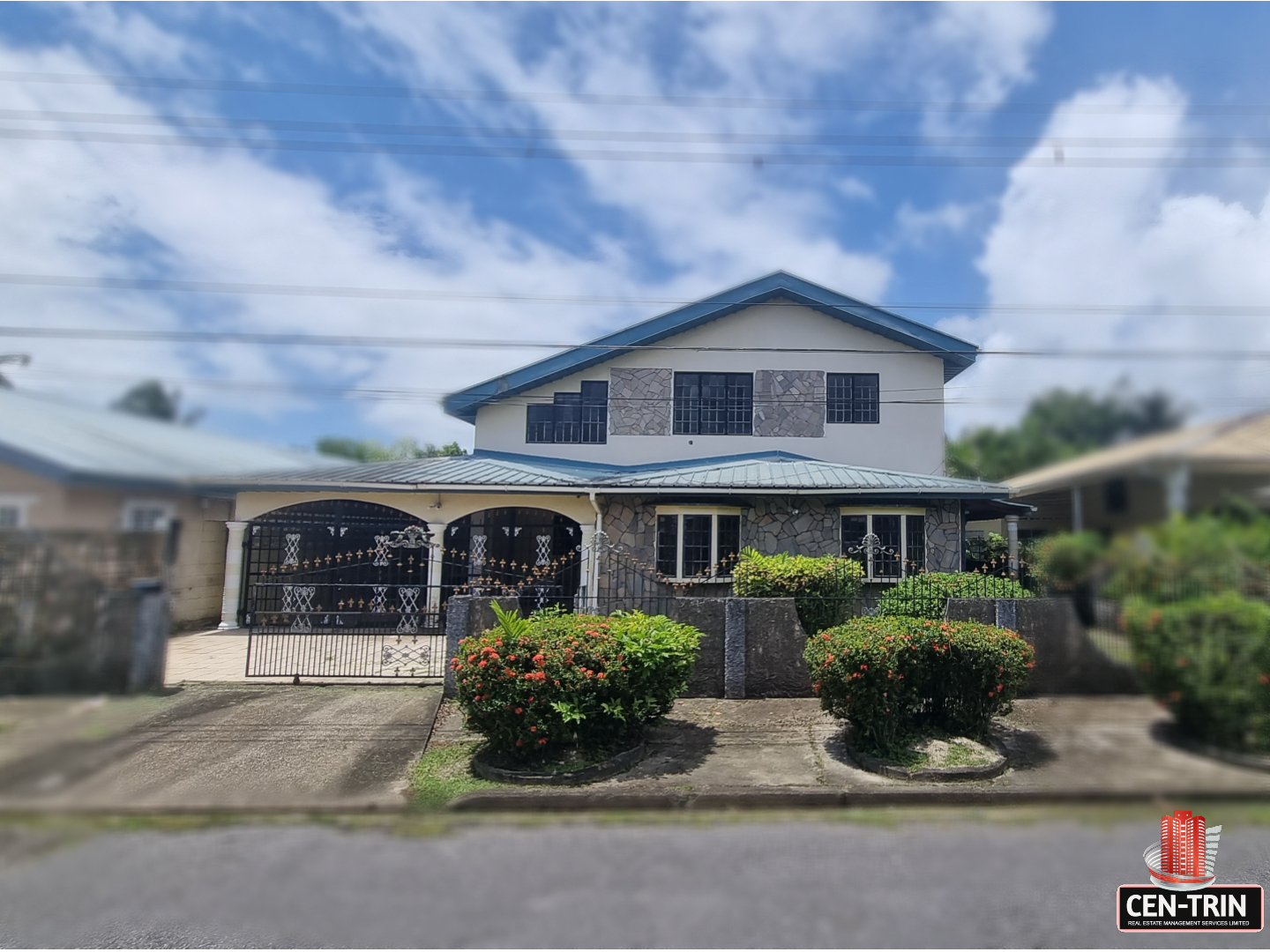A two-story Property for sale in Santa Rosa with a blue roof, stone accents on the first floor, and a black wrought-iron gate, set back from the street.