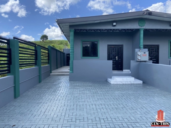 A modern, two-year-old Barrackpore Duplex for Sale featuring a grey exterior with green trim and a paved driveway. The property is secured by a black metal fence with razor wire and is part of a Smart Home Trinidad security system, representing a prime Trinidad Investment Property suitable for Trinidad Airbnb Property revenue. Note the paved parking area and clear, well-maintained entrance.